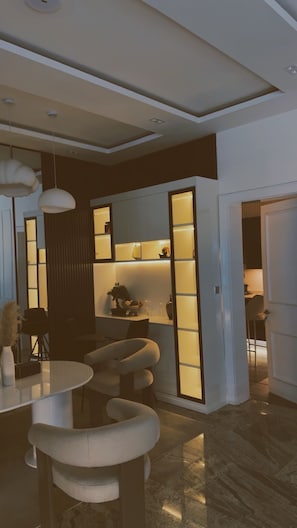 A modern interior with a dining area featuring a round table and chairs, a kitchen with cabinets, and a sliding door leading to another room. - Smart Luxury 2BR | Starlink • PS5 • 24/7 Power • Modern Living (Abuja)