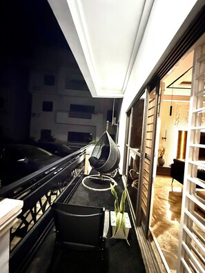 A balcony with a hanging chair, a small table, and a potted plant. - Smart Luxury 2BR | Starlink • PS5 • 24/7 Power • Modern Living (Abuja)