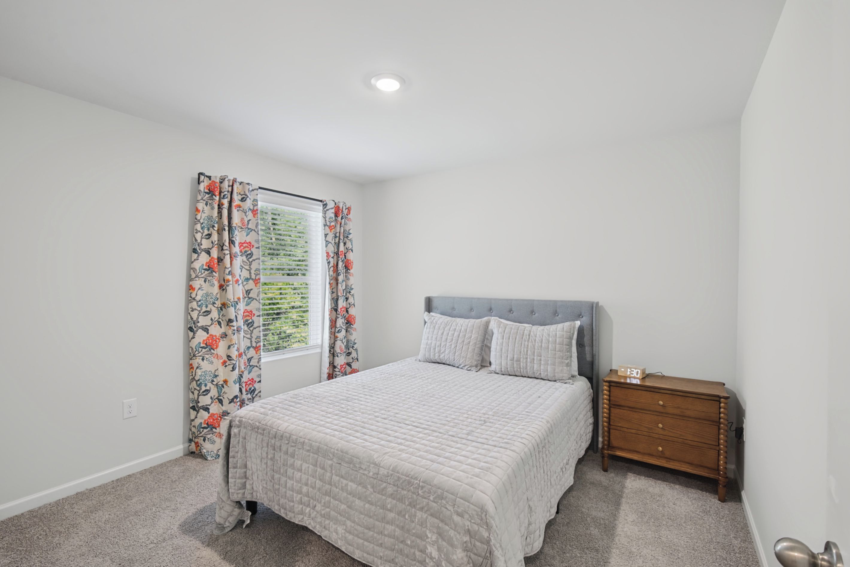 A bedroom with a bed, a nightstand, a window with curtains, and a ceiling light.