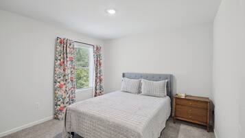A bedroom with a bed, a nightstand, a window with curtains, and a ceiling light.