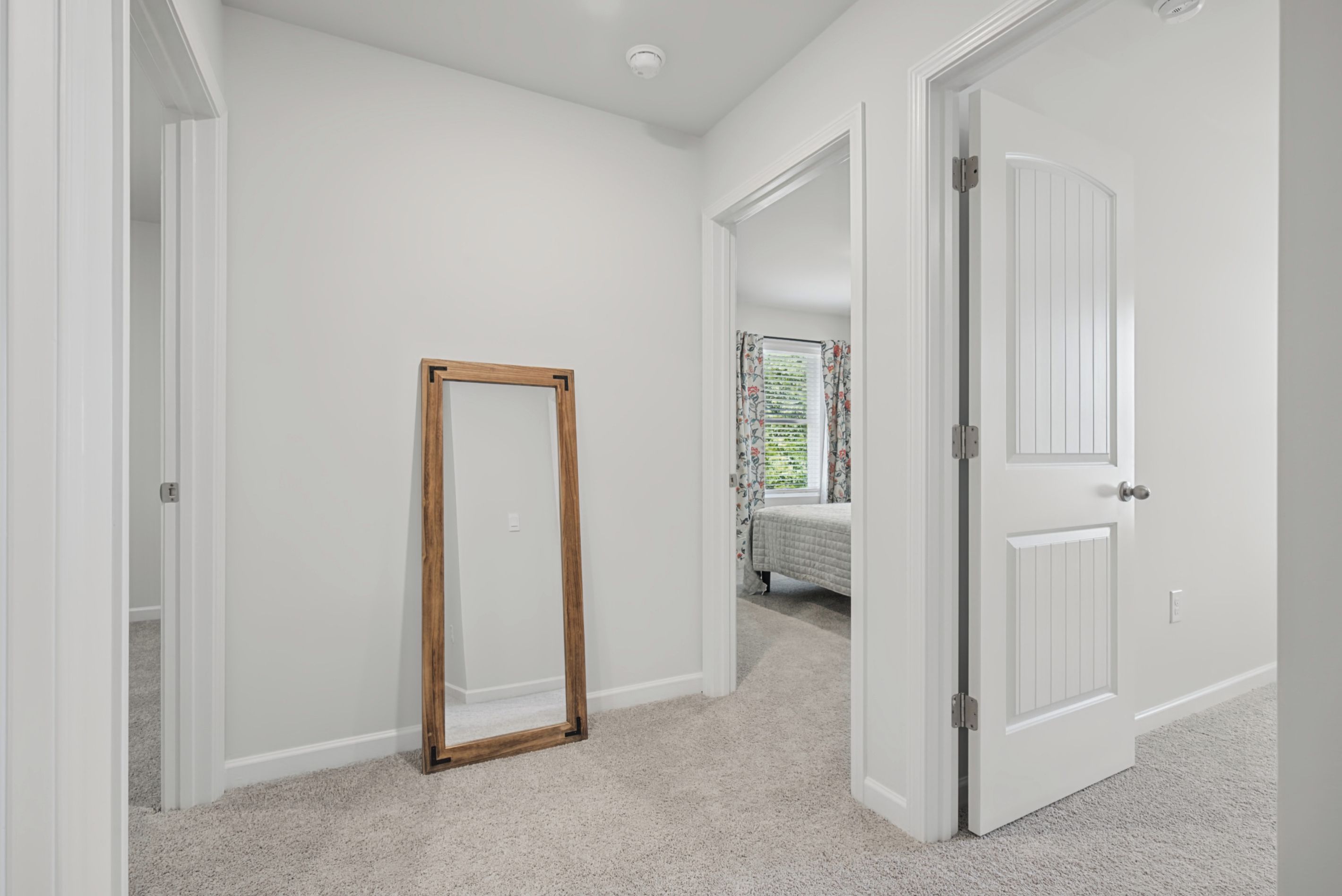 A hallway with a wooden frame leaning against the wall, a door, and a window with floral curtains.