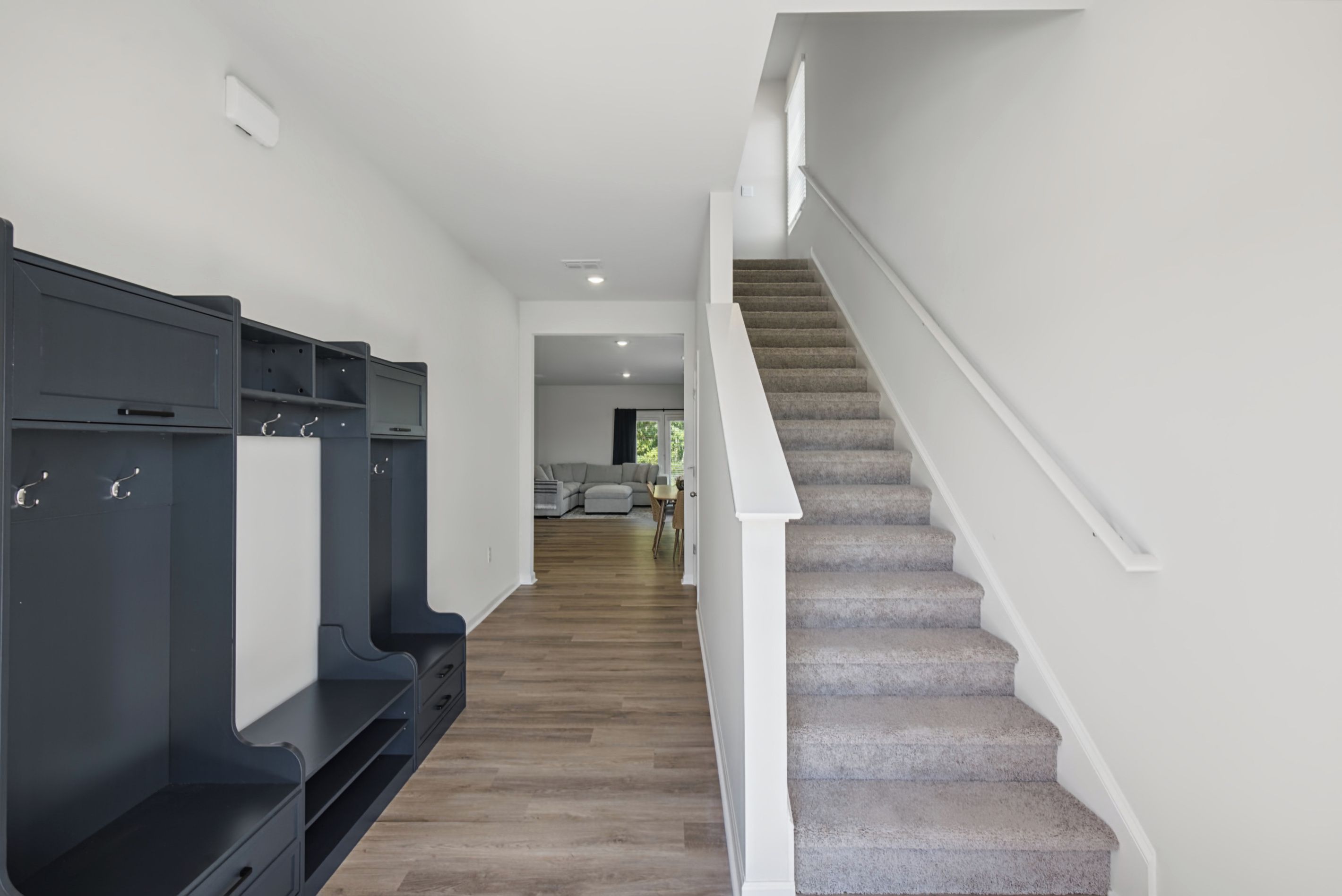 A hallway with a staircase leading to a living area, featuring a dark-colored storage unit and a carpeted staircase.