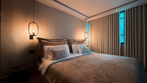 Ein Schlafzimmer mit einem großen Bett, zwei Wandleuchten und einem Fenster mit vertikalen Rollläden.