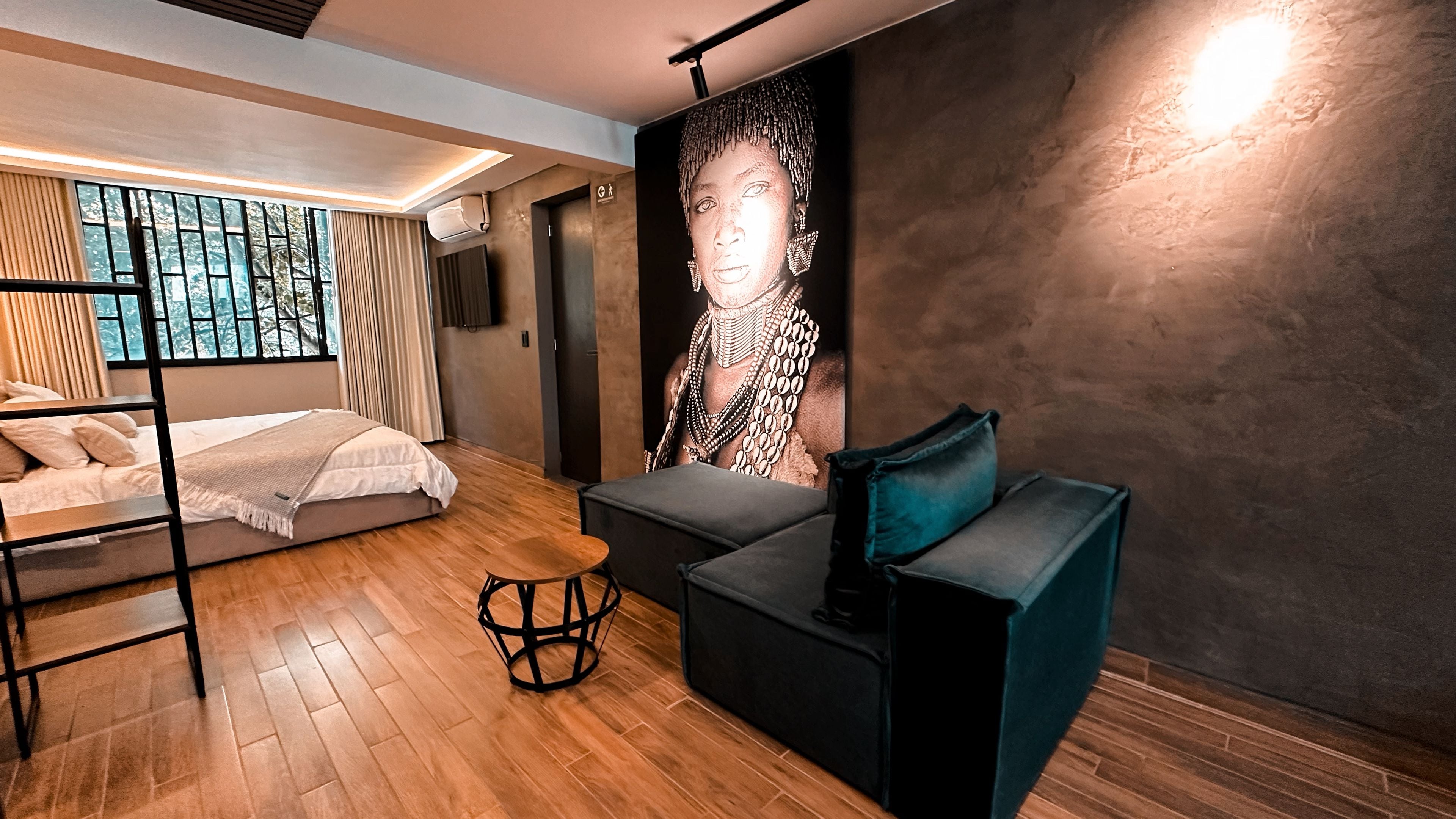 A modern bedroom with a bunk bed, a sofa, a wall-mounted TV, and a large abstract painting.