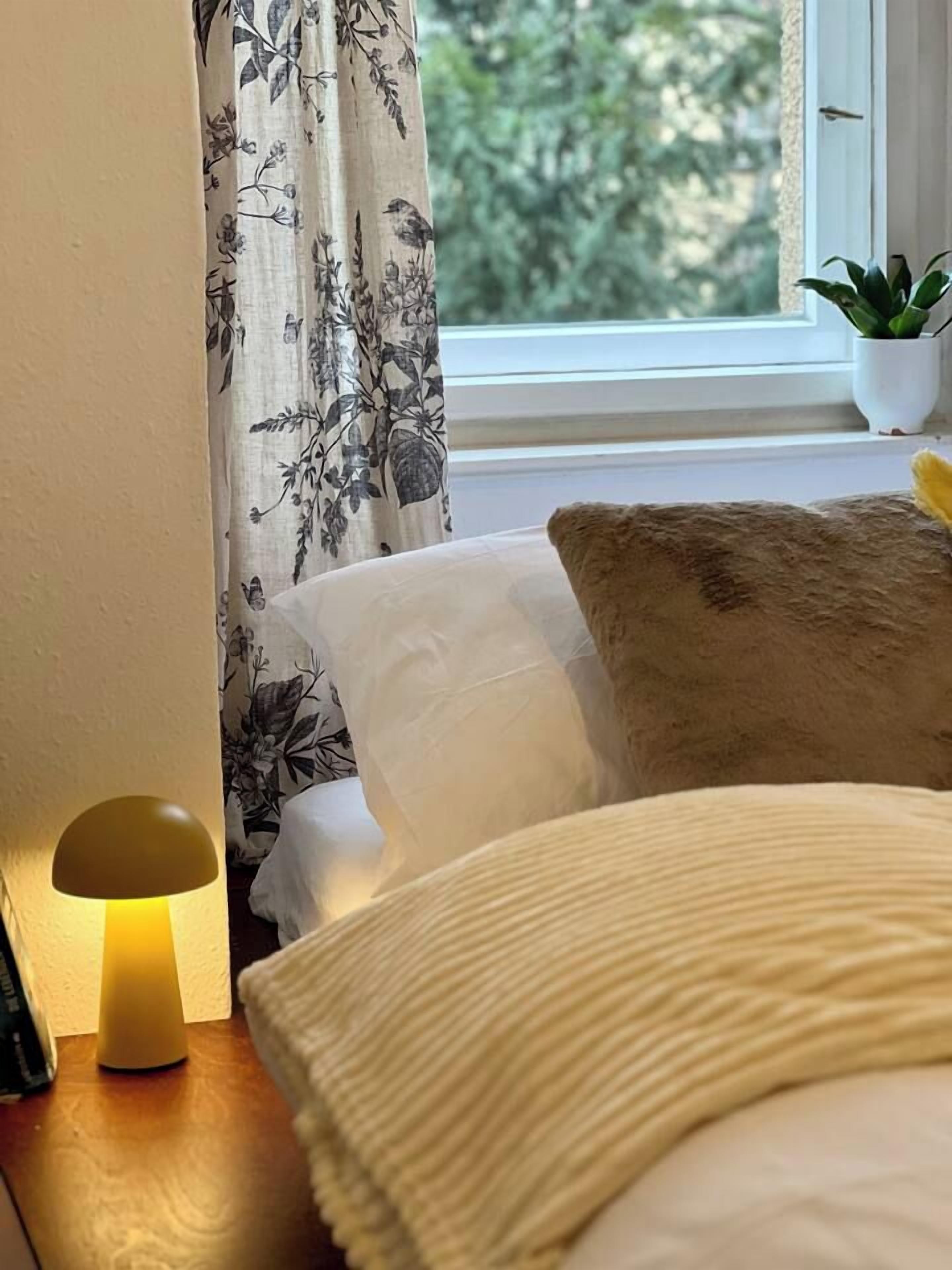 Ein Schlafzimmer mit einem Bett, einer Lampe, einem Fenster mit Blick und einer Topfpflanze.