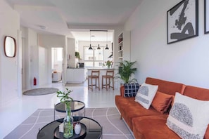 A modern living room with a sofa, a coffee table, and a dining area in the background. - Design Apart 1 BR/Pankow-P. Berg/Netflix/Parking (Berlin-Bezirk Pankow)