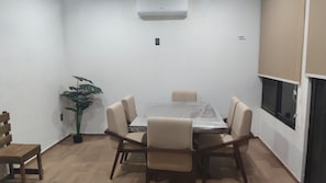 Zona de menjador amb taula, cadires, una planta en test i un aparell d'aire condicionat.
