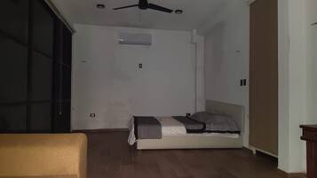 Ein Zimmer mit einem Bett, einem Deckenventilator, einer Schiebetür und Holzboden.