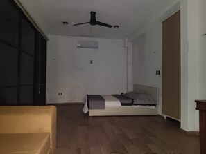 Une pièce avec un lit, un ventilateur de plafond, une porte coulissante et un plancher en bois.