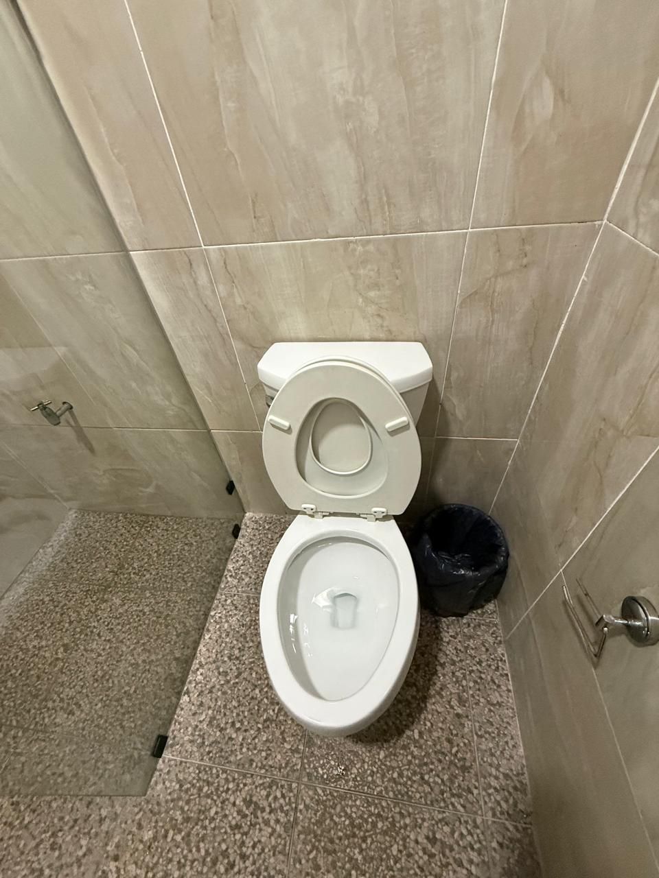 A bathroom with a white toilet, a black trash bin, and a tiled floor.