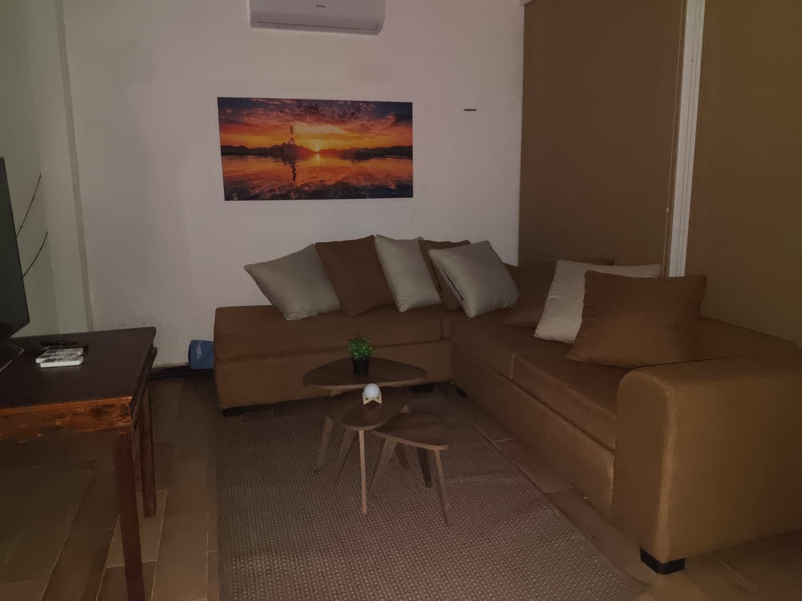 A living room with a brown sofa, a coffee table, and a painting of a sunset.