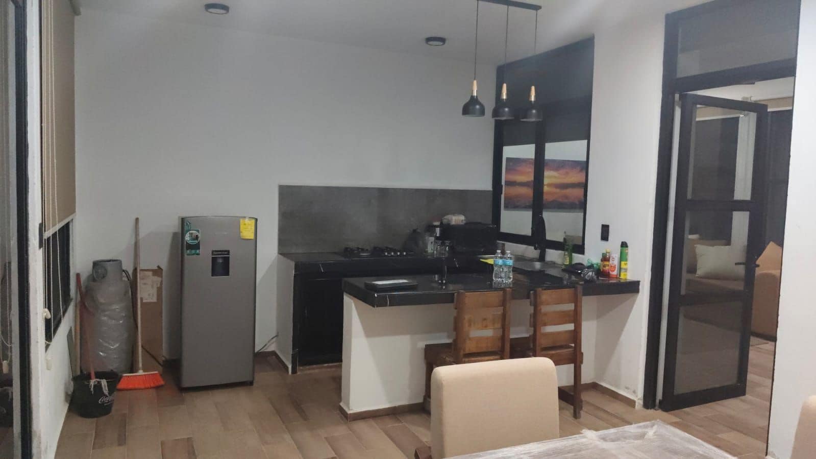 Eine kompakte Küche mit Kühlschrank, Herd und Spüle. Zwei Stühle und ein kleiner Tisch sind vorhanden.