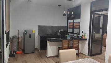 Eine kompakte Küche mit Kühlschrank, Herd und Spüle. Zwei Stühle und ein kleiner Tisch sind vorhanden.