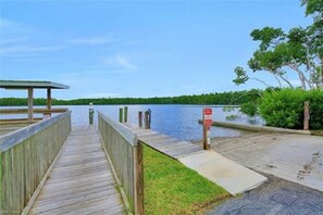 A wooden pier leading to a dock with a signpost, surrounded by greenery and a calm body of water. - Snook Shack - 3 Bedroom/2 Bath Condo Located in Historic Everglades City (Everglades City)