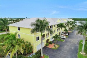 A multi-story building with a parking area and palm trees.