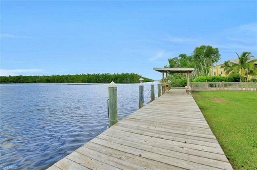 A wooden dock extending into calm water, with a covered structure and a fence on the right.