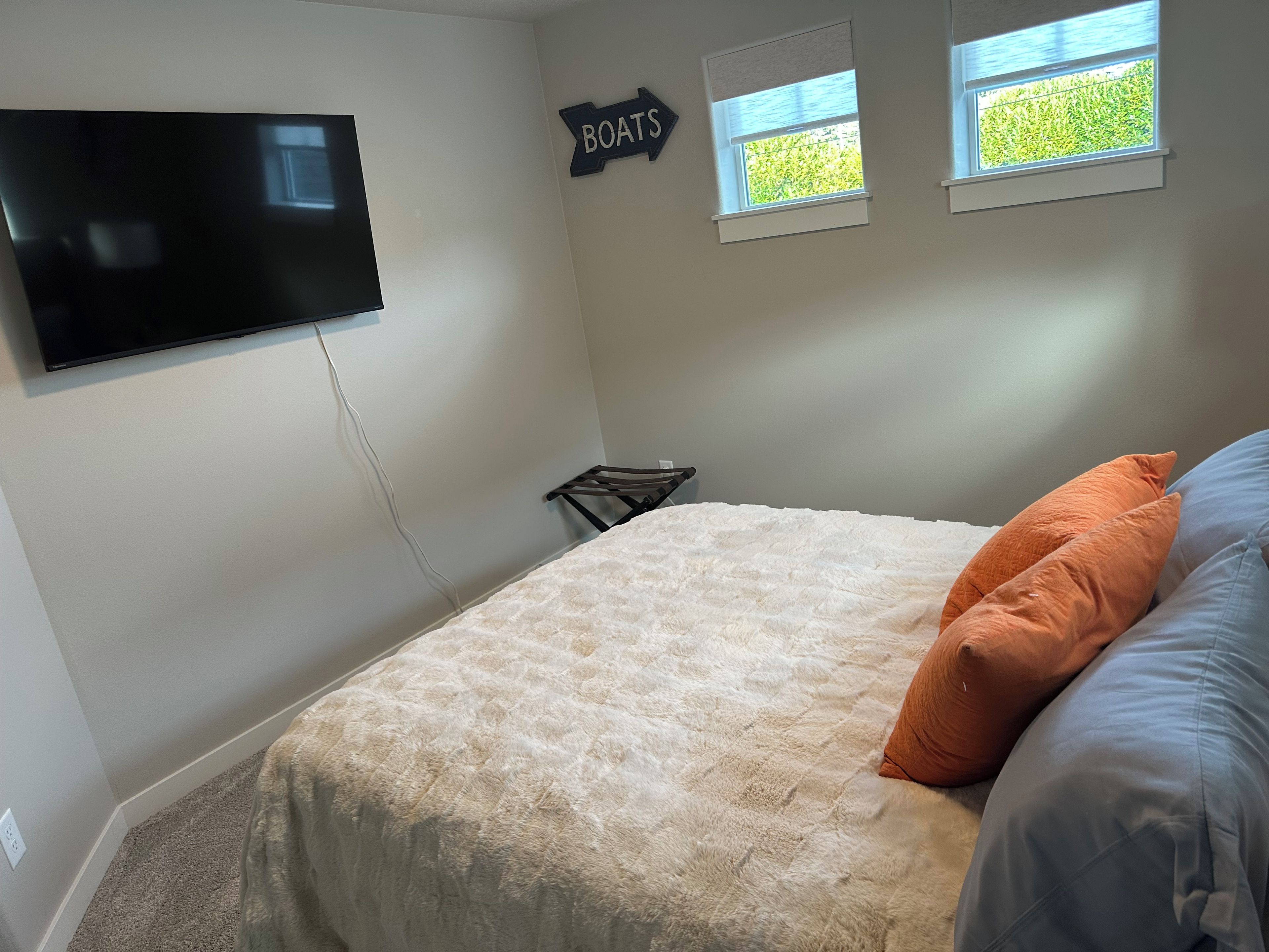 A bedroom with a bed, a TV mounted on the wall, a window, and a sign that says 'BOATS'.