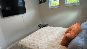 A bedroom with a bed, a TV mounted on the wall, a window, and a sign that says 'BOATS'.