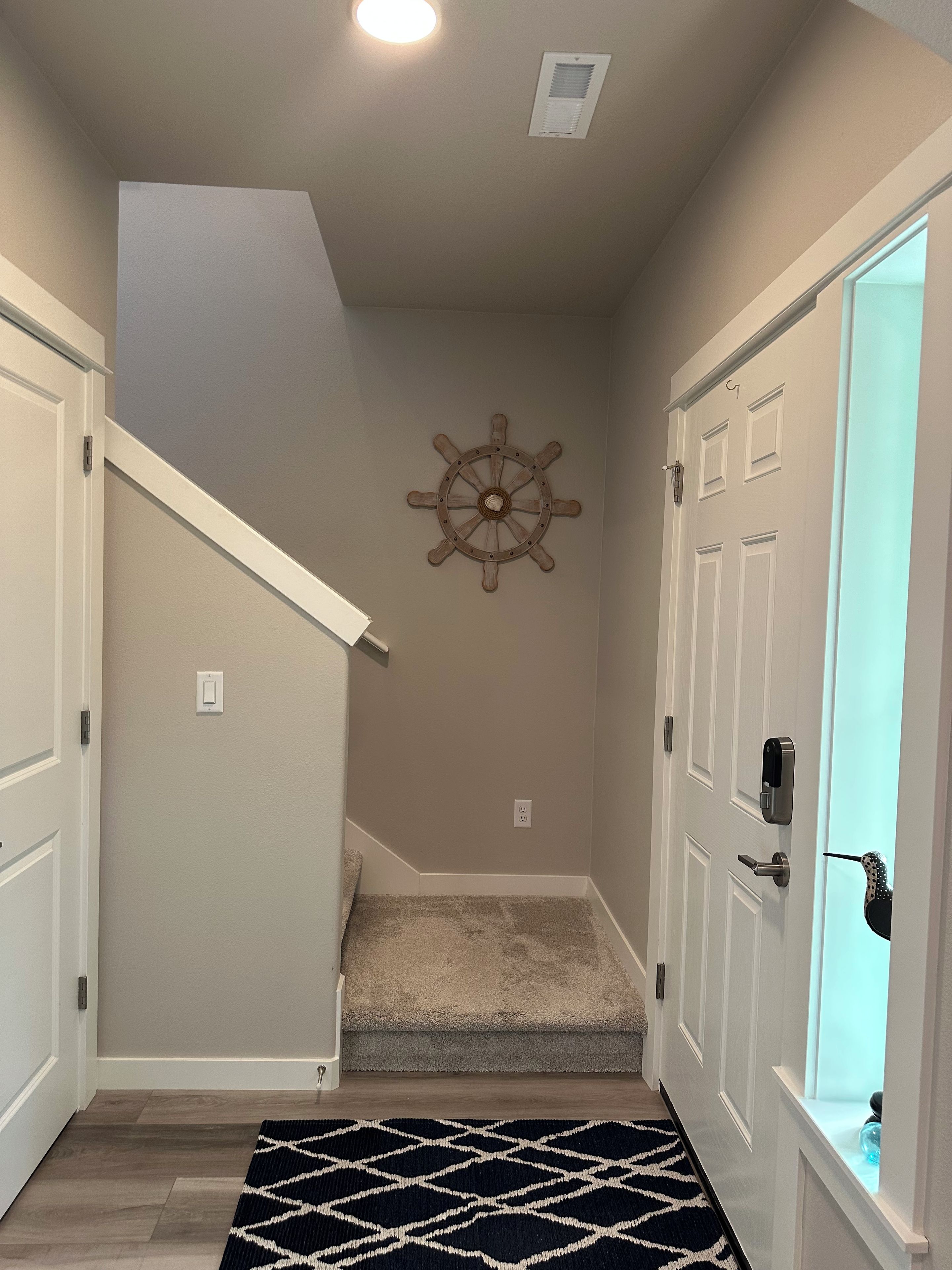 A hallway with a carpet, a wall-mounted ship's wheel decoration, and a door with a key lock.