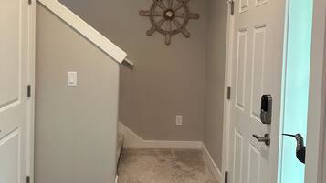 A hallway with a carpet, a wall-mounted ship's wheel decoration, and a door with a key lock.