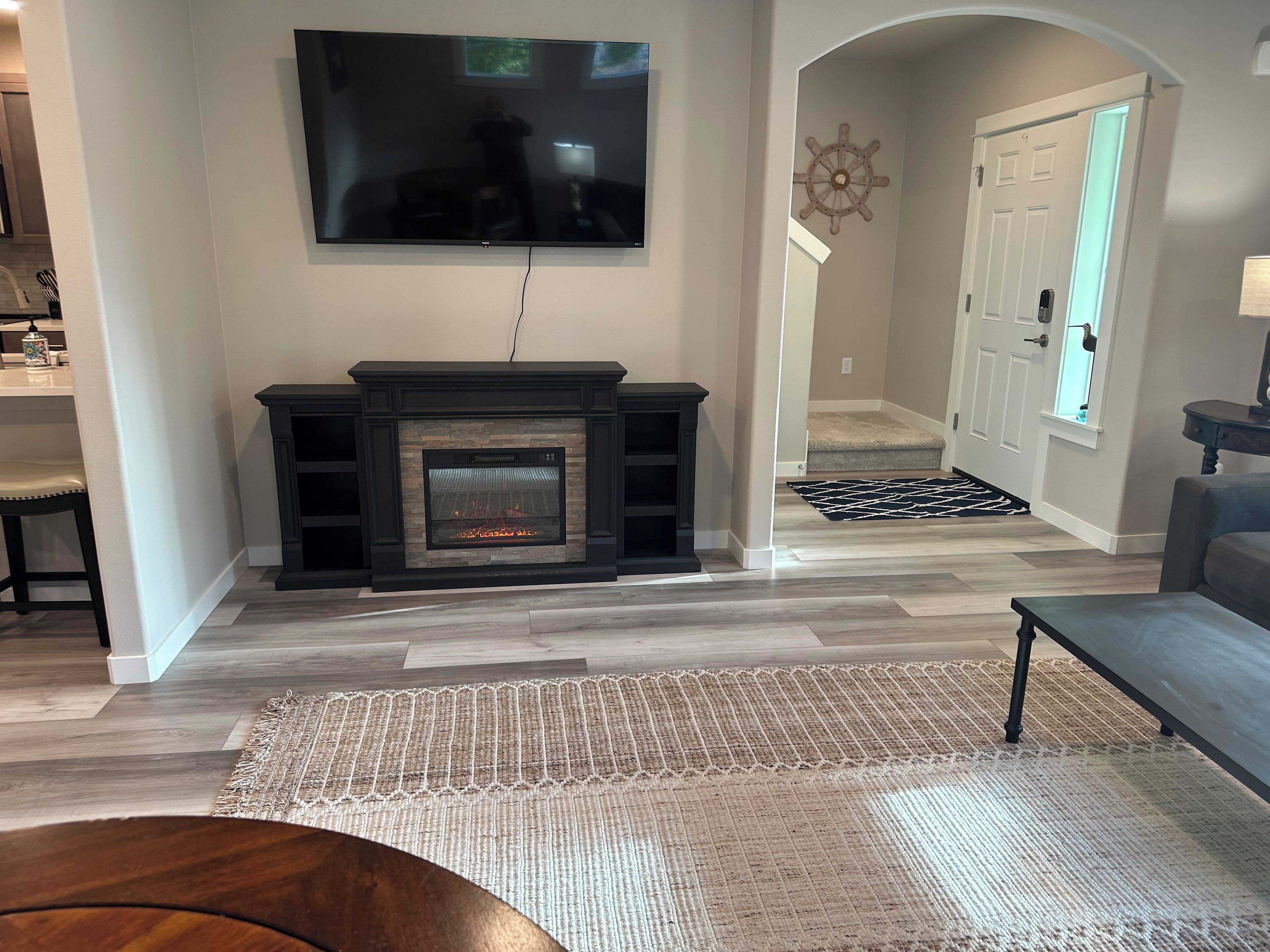 A living room with a fireplace, a television mounted on the wall, and a hallway leading to a door.