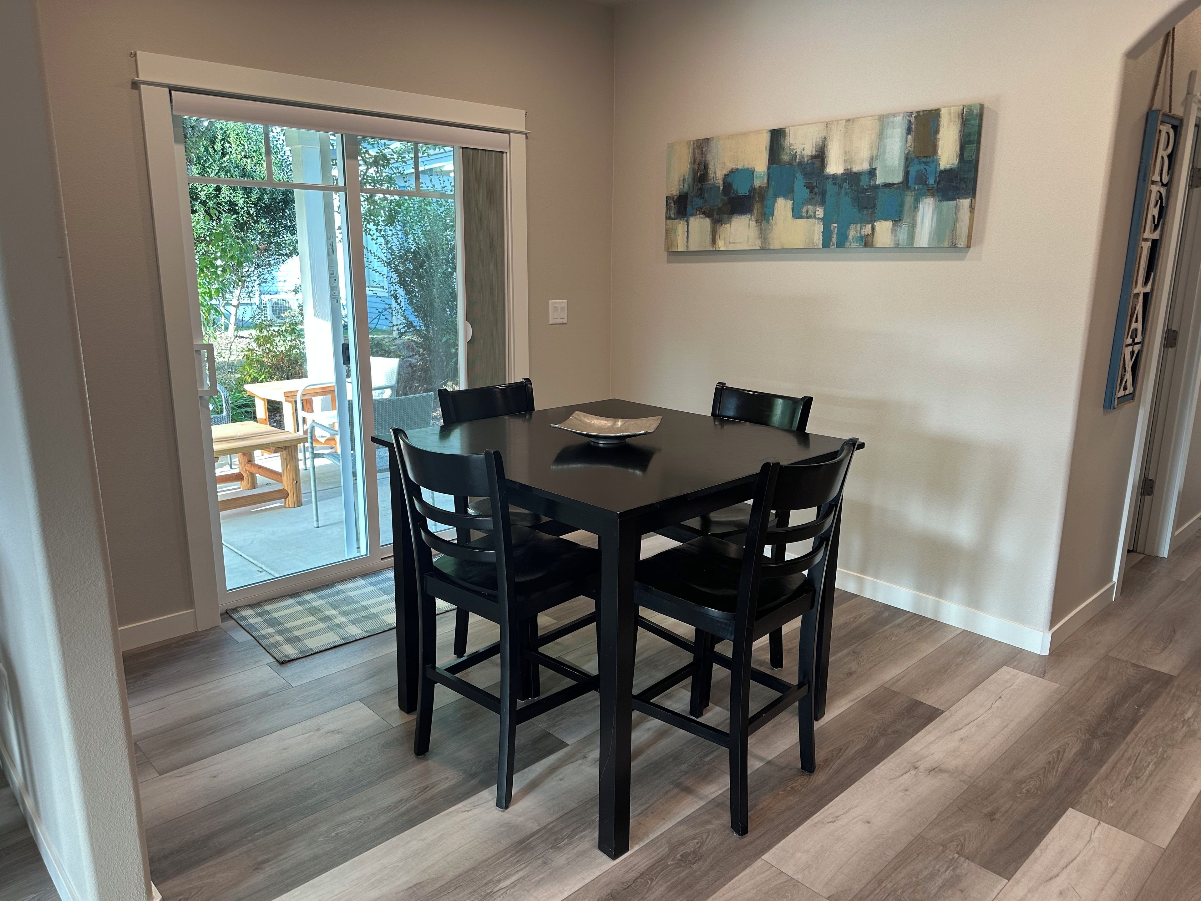 A dining area with a table and chairs, a sliding glass door leading to an outdoor patio, and a piece of abstract art on the wall.