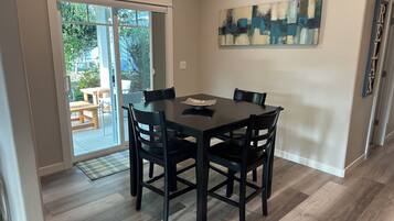 A dining area with a table and chairs, a sliding glass door leading to an outdoor patio, and a piece of abstract art on the wall.