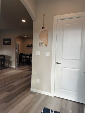 A hallway with a white door, a wall-mounted sign reading 'THE BEACH,' and a dining area with chairs and a table.