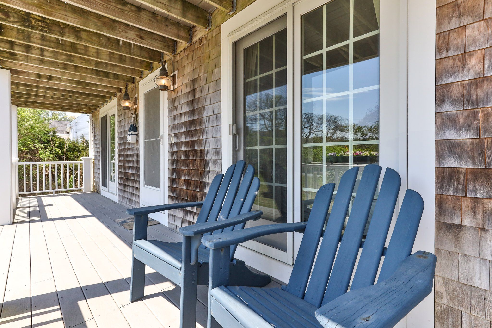 A covered porch with Adirondack chairs and a wooden exterior wall.