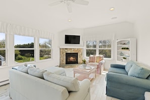 A spacious living room with a stone fireplace, large windows, and a flat-screen TV. - East Sandwich House| Slps 8 | 3Beds2Baths (East Sandwich)