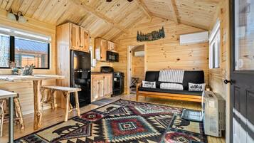 Een gezellig blokhutinterieur met een houten plafond, een keuken met apparatuur, een bank met een welkomstmat en een kamerbreed tapijt.