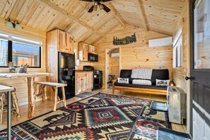 Een gezellig blokhutinterieur met een houten plafond, een keuken met apparatuur, een bank met een welkomstmat en een kamerbreed tapijt.