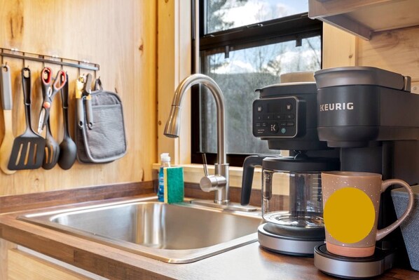 Una cocina con una cafetera, una taza y varios utensilios sobre la encimera.