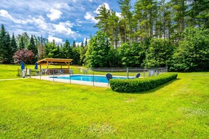 Una piscina con un deck amurallado, rodeada de césped y árboles bien cuidados.