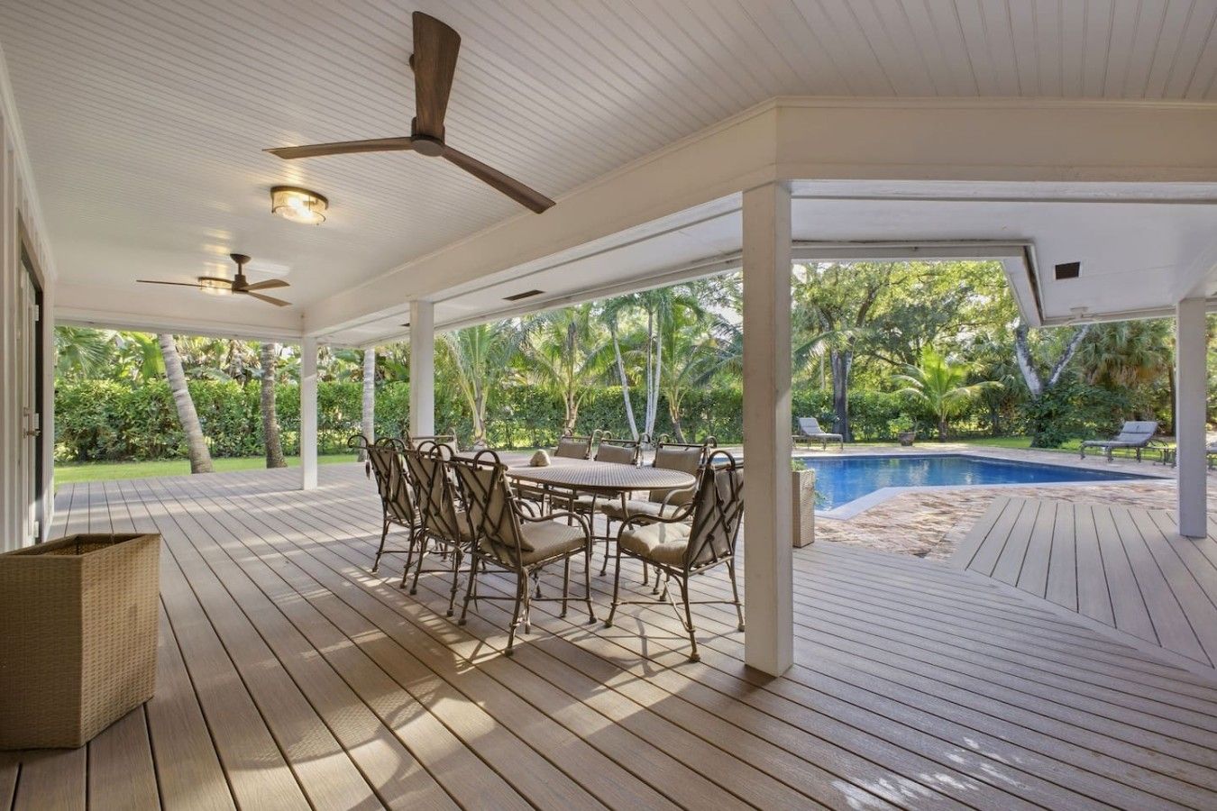 A covered outdoor area with a pool, wooden deck, and a table with chairs.
