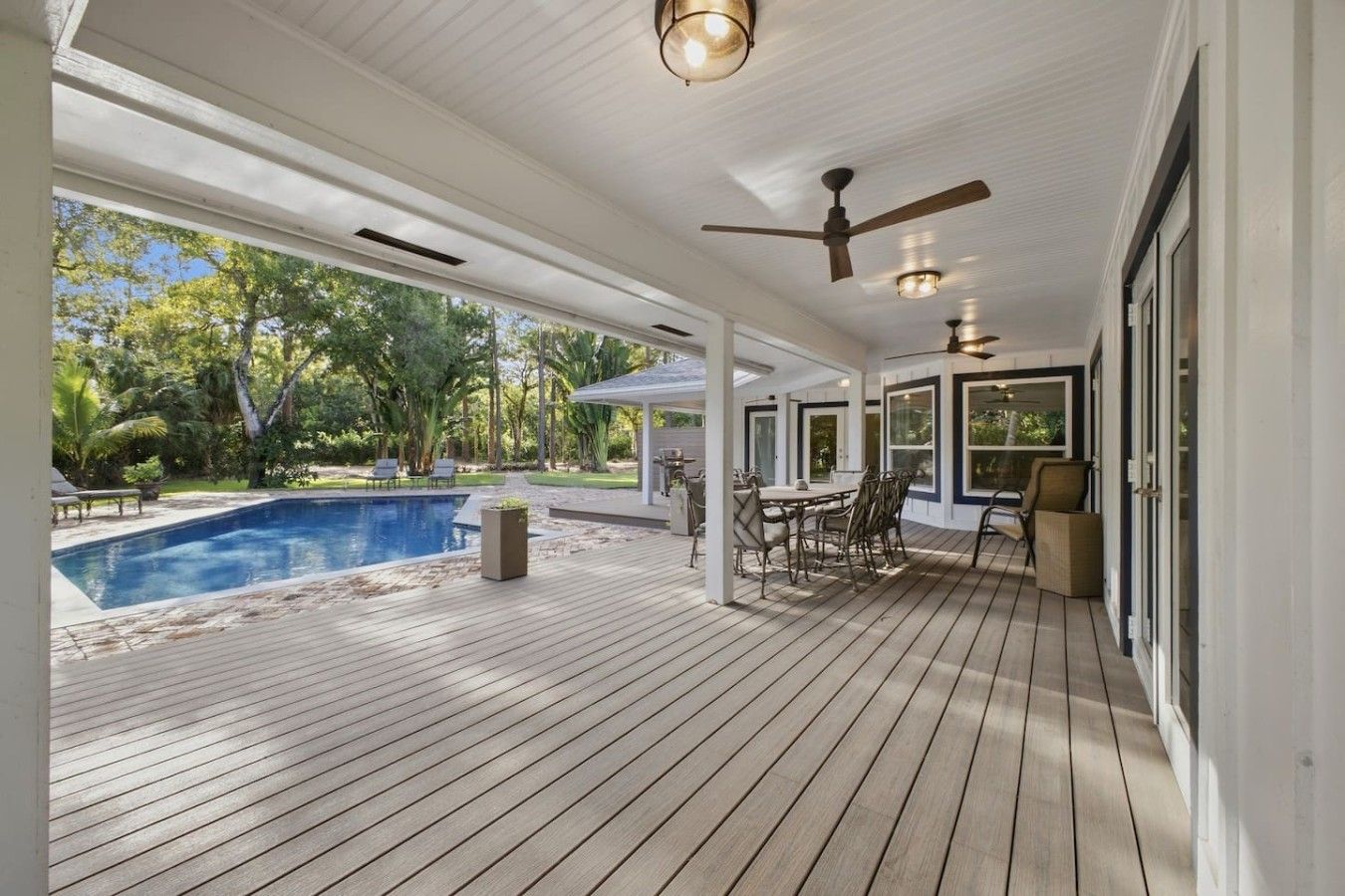 A covered outdoor area with a pool, seating, and ceiling fans.