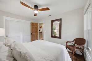 Un dormitorio con una cama, una silla, un ventilador de techo y un espejo.