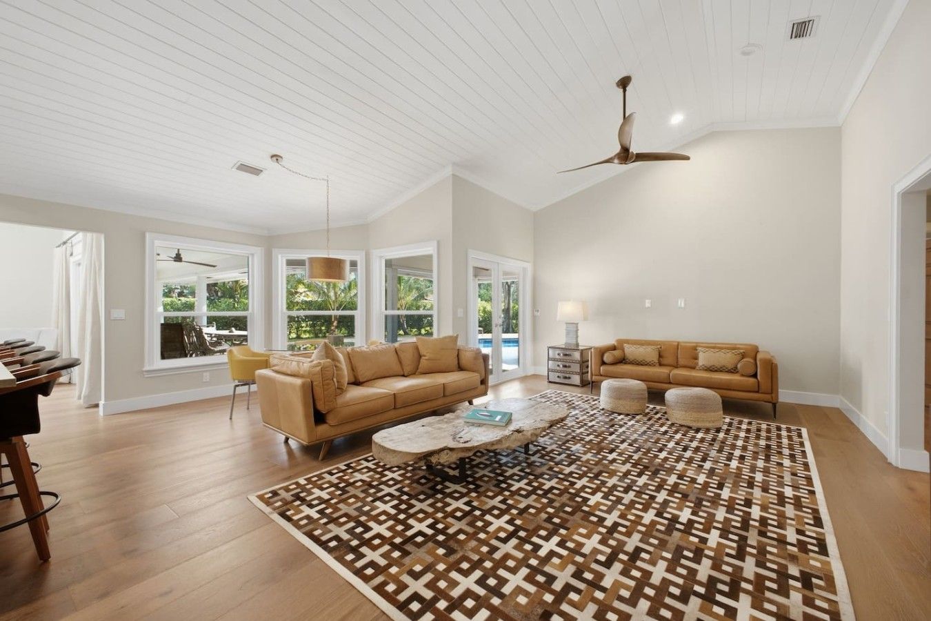 A spacious living room with a high ceiling, large windows, a ceiling fan, and a patterned rug.