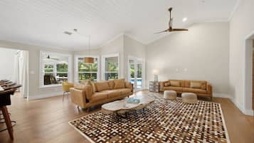 A spacious living room with a high ceiling, large windows, a ceiling fan, and a patterned rug.