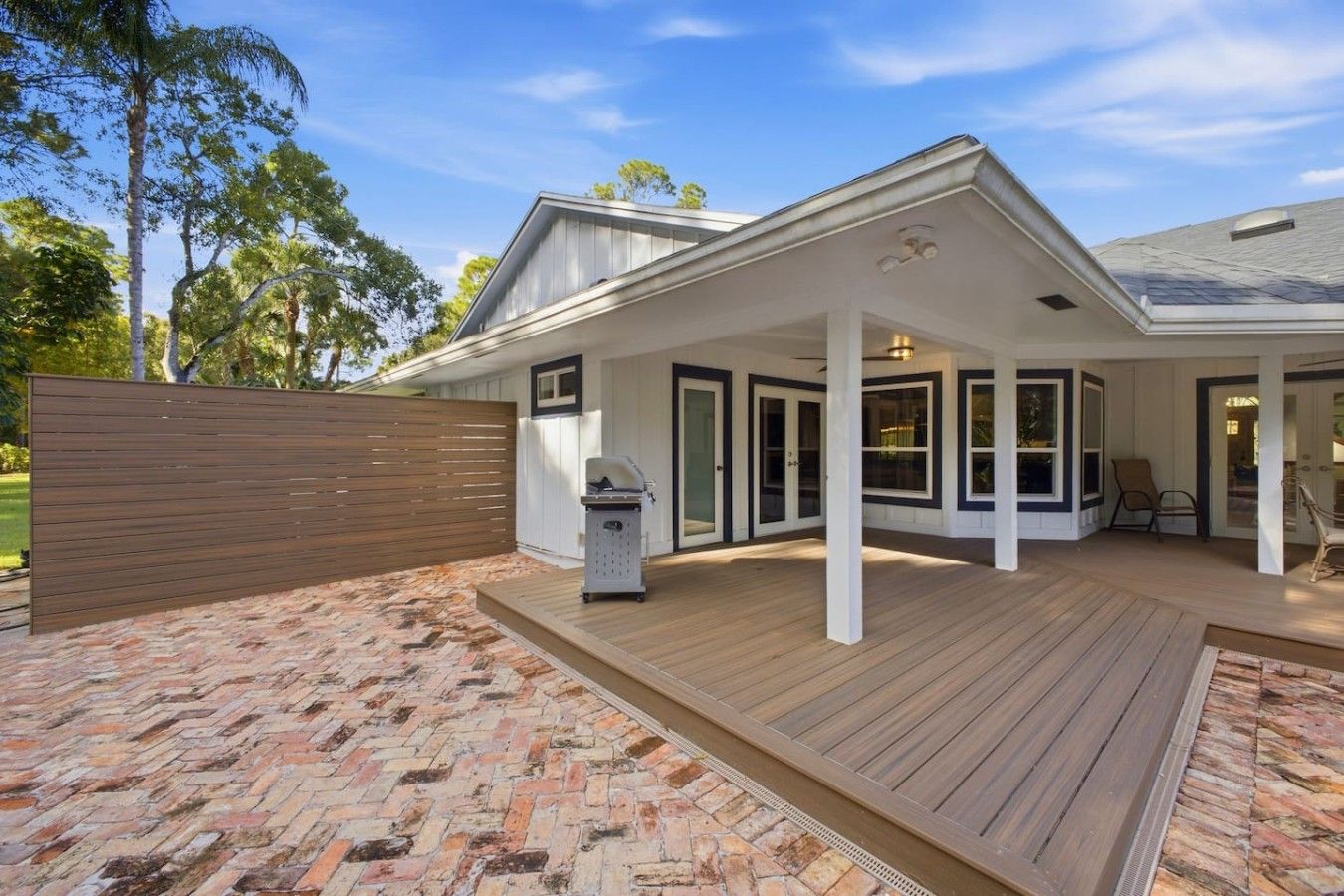 A covered outdoor patio area with a brick floor, a wooden deck, and a grill station.