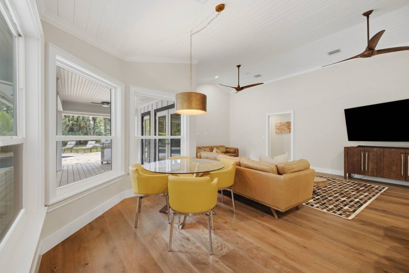 A modern living room with a round glass table, yellow chairs, a brown sofa, and a flat-screen TV.