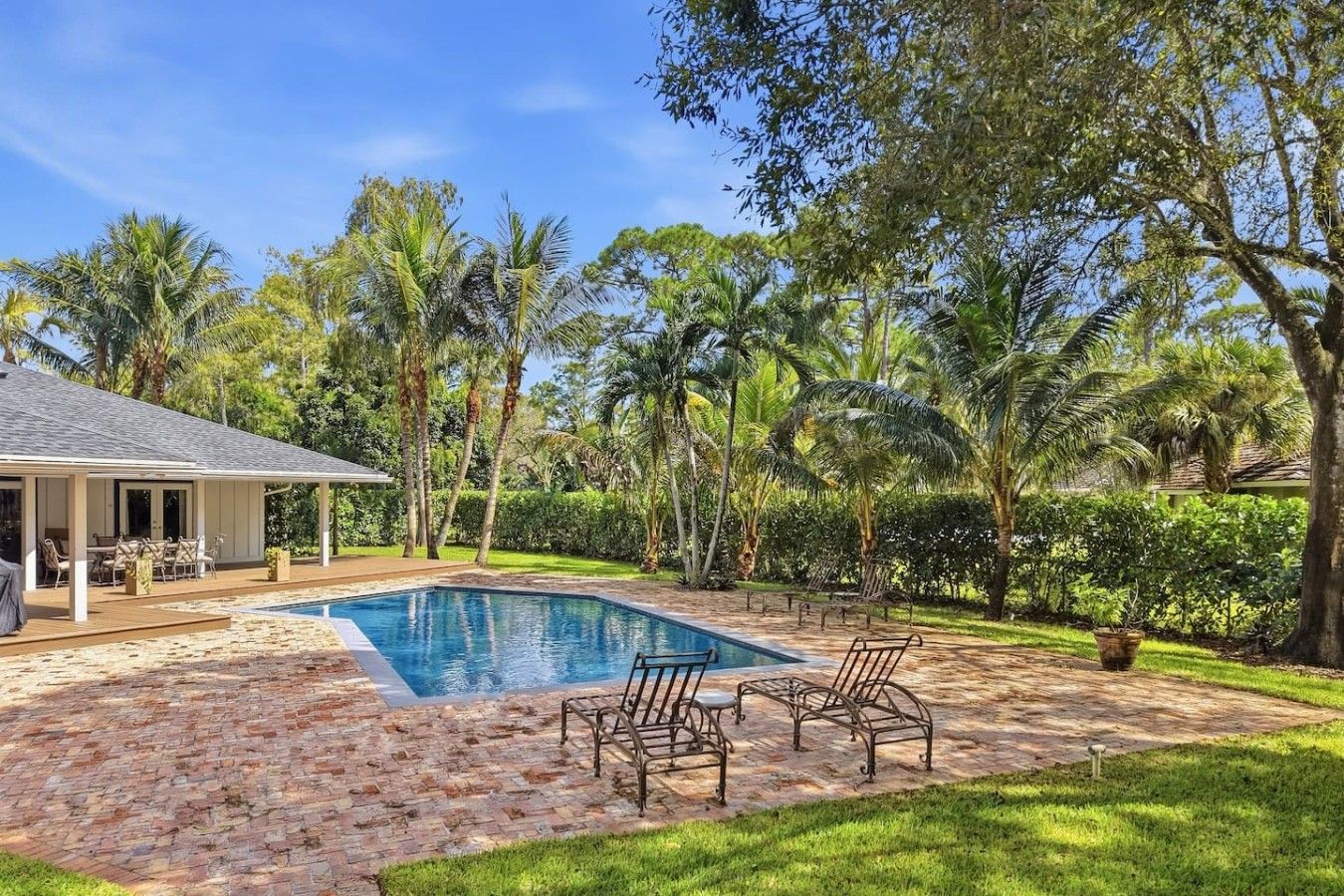 A swimming pool with a deck area, surrounded by palm trees and a covered patio.