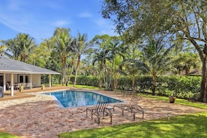 Una piscina con zona de terraza, rodeada de palmeras y un porche cubierto.