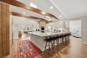 A modern kitchen with a large island, bar stools, and a rustic brick accent wall. - Wellington Equestrian Escape | Ranch w/ Pool (Wellington)