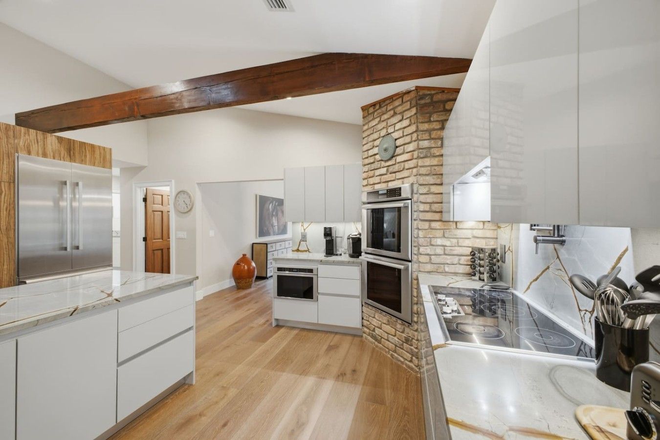 A modern kitchen with white cabinetry, a stone accent wall, and a wooden ceiling beam.