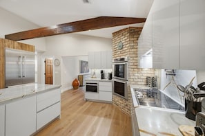 A modern kitchen with white cabinetry, a stone accent wall, and a wooden ceiling beam. - Wellington Equestrian Escape | Ranch w/ Pool (Wellington)