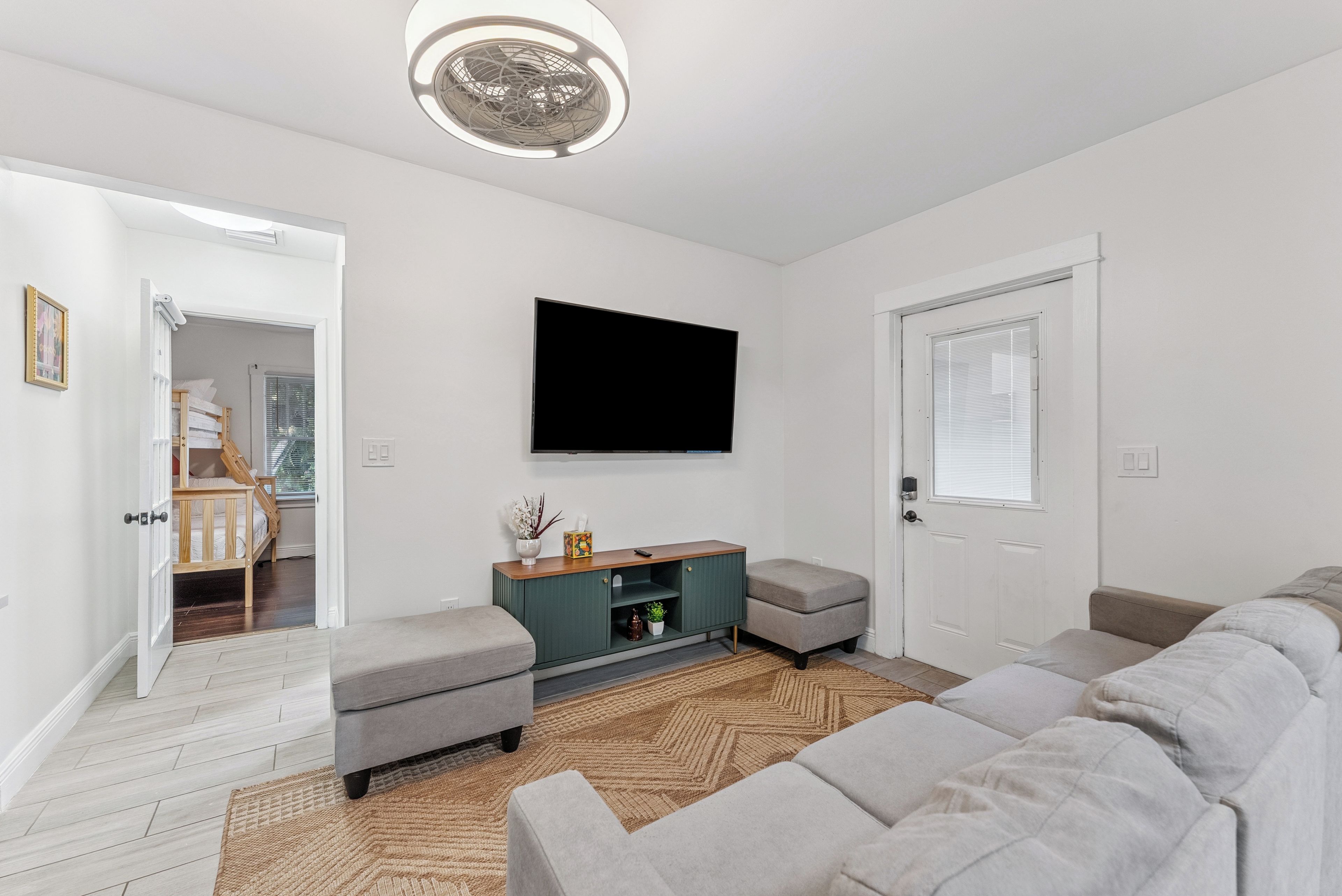 A modern living room with a grey sofa, a wooden cabinet, and a flat-screen TV mounted on the wall.