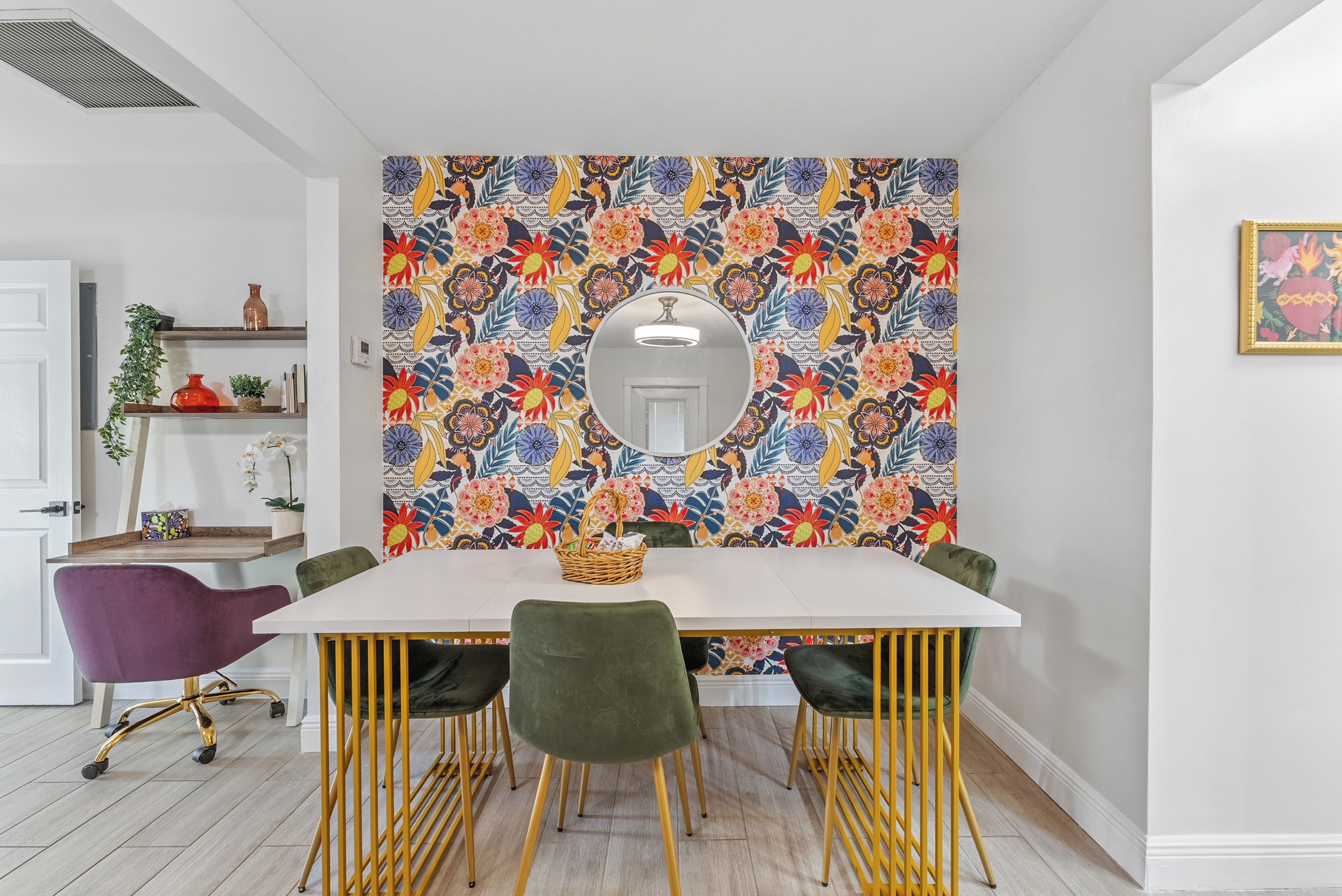 A dining area with a white table, green chairs, and a colorful floral wall mural.