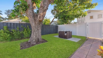 A backyard with a tree, a patio table, and a white fence.