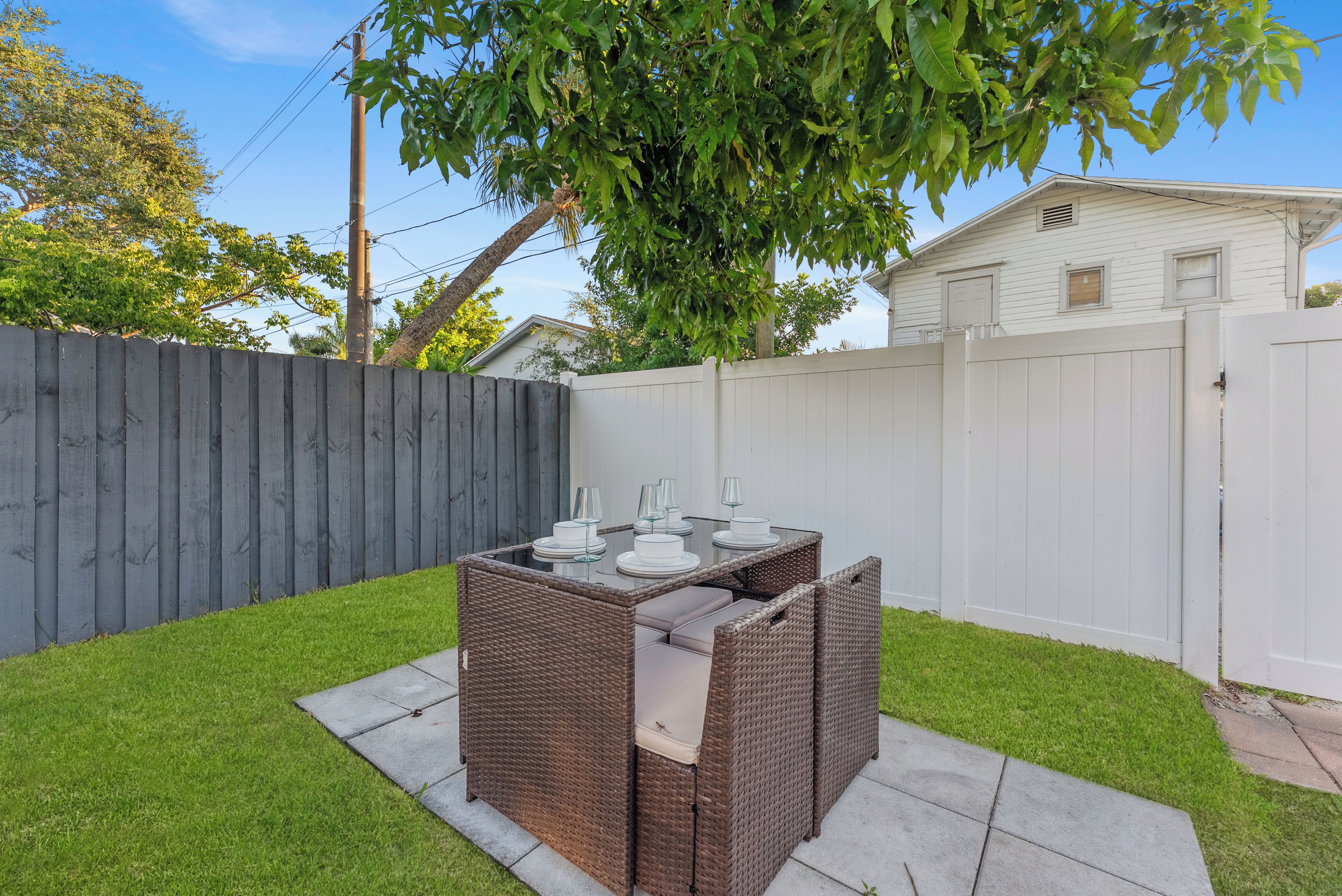A backyard with a dining table and chairs, surrounded by a white fence and a wooden fence.